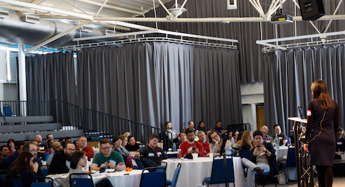 A group of people sat down in a conference room. There is a woman at the front running the workshop. 