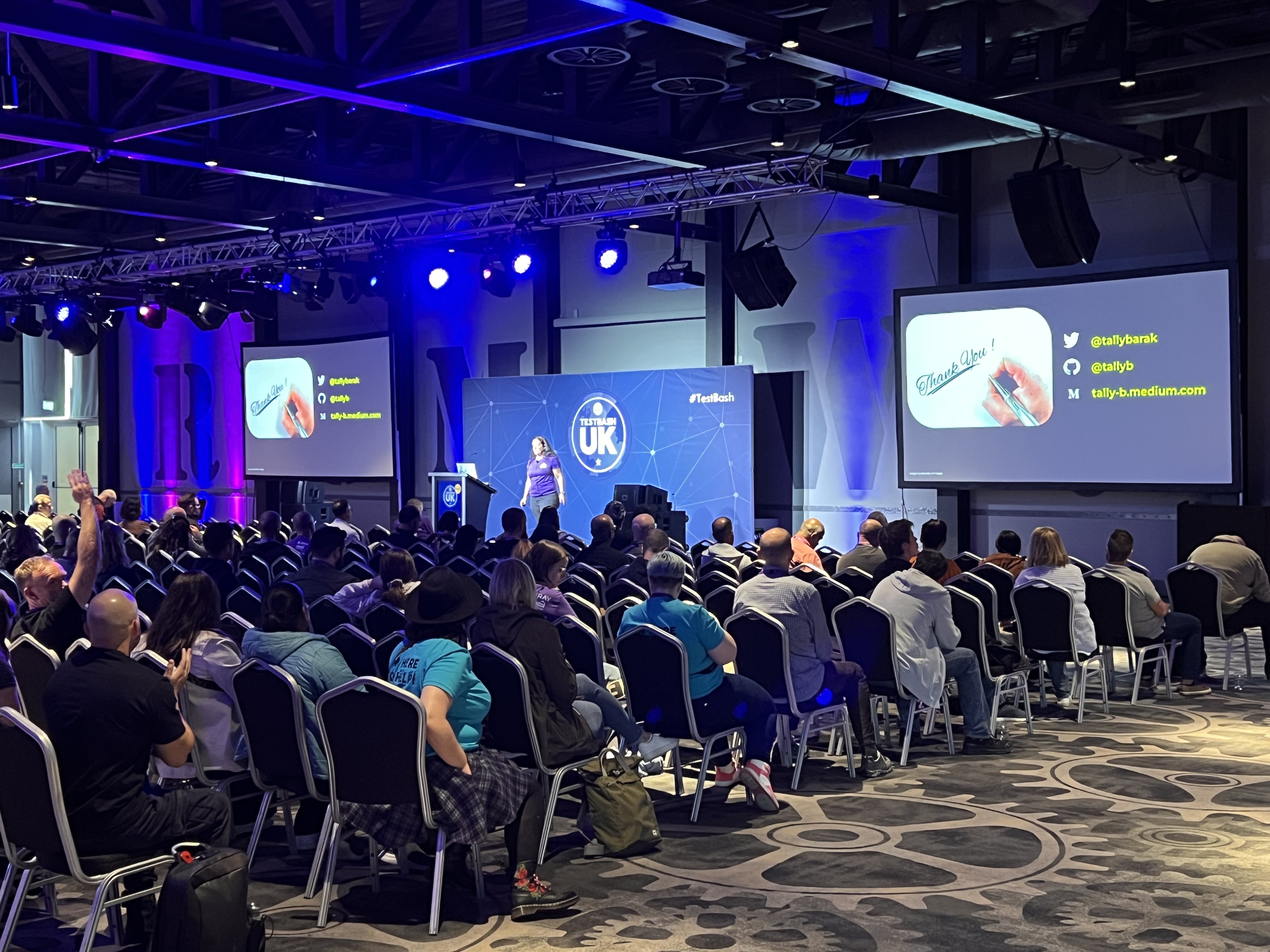A conference room full of many people. There is a woman on stage. 