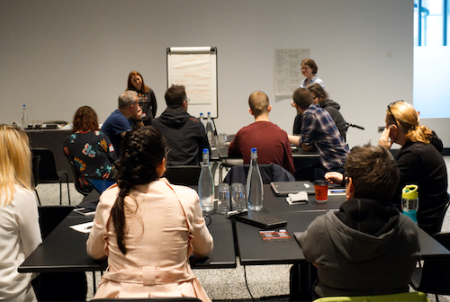 A group of people sat down in a conference room. There are two people at the front running the workshop. 