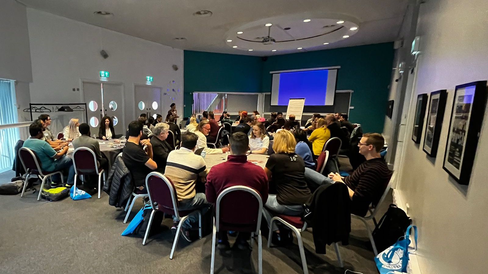 A group of people sat at desks in a conference workshop room.