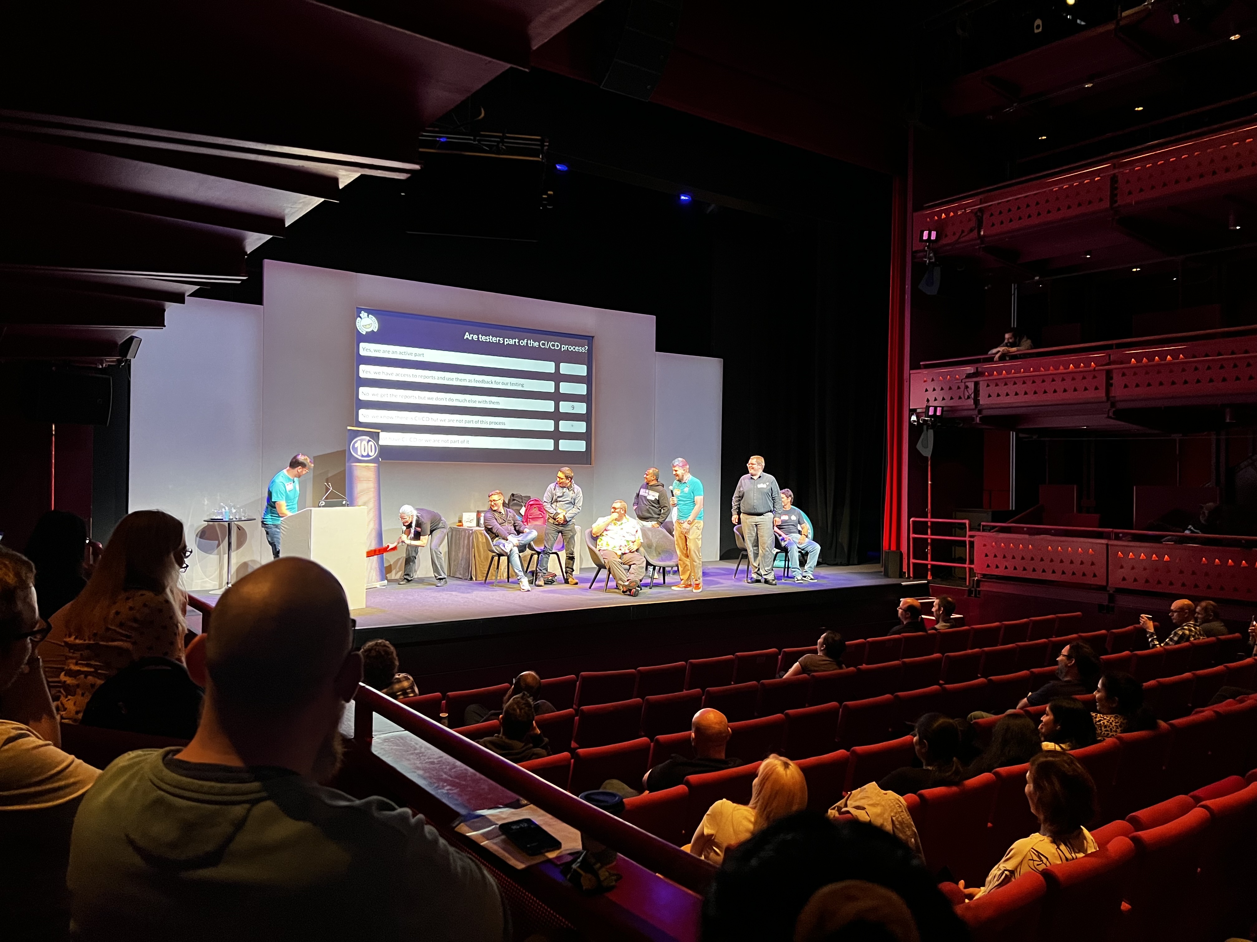 A group of people in a conference hall. There are multiple people on stage playing a fun game.