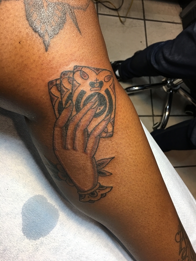 A photo of a woman's leg with a tattoo of cards that includes the Ministry of Testing logo