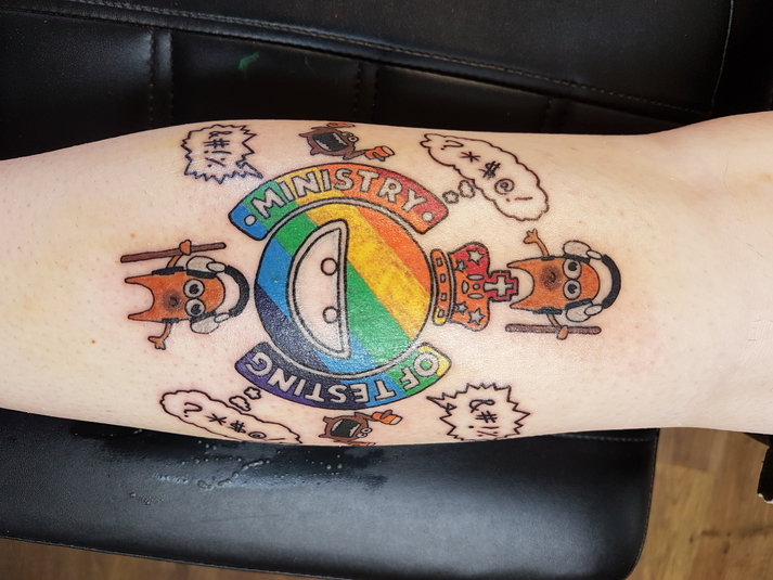 A photo of an arm with a rainbow coloured Ministry of Testing logo tattoo